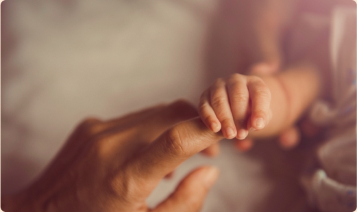 A photo of an adult hand reaching out towards a baby, and the baby's hand wrapped loosely around the adult's index finger.