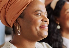 Photo of a dark-skinned woman wearing an orange hair wrap smiling